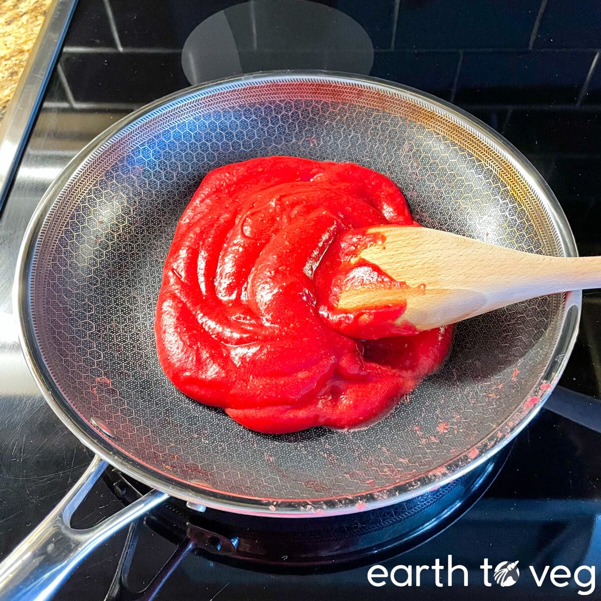 A wooden spatula is immersed in a bright red hawthorn berry puree on a nonstick pan.