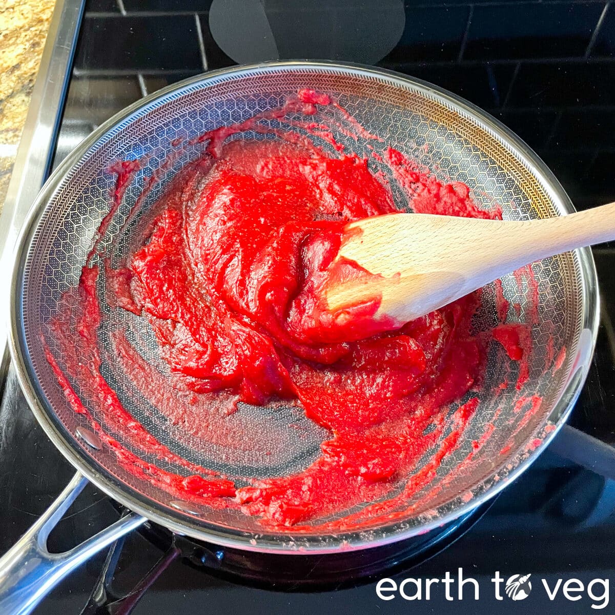 A wooden spatula stirring thickened hawberry puree in a nonstick Hexclad pan.