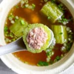 spoon holding up a stuffed bitter gourd over a pot full of Thai bitter melon soup