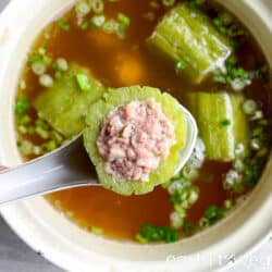 spoon holding up a stuffed bitter gourd over a pot full of Thai bitter melon soup