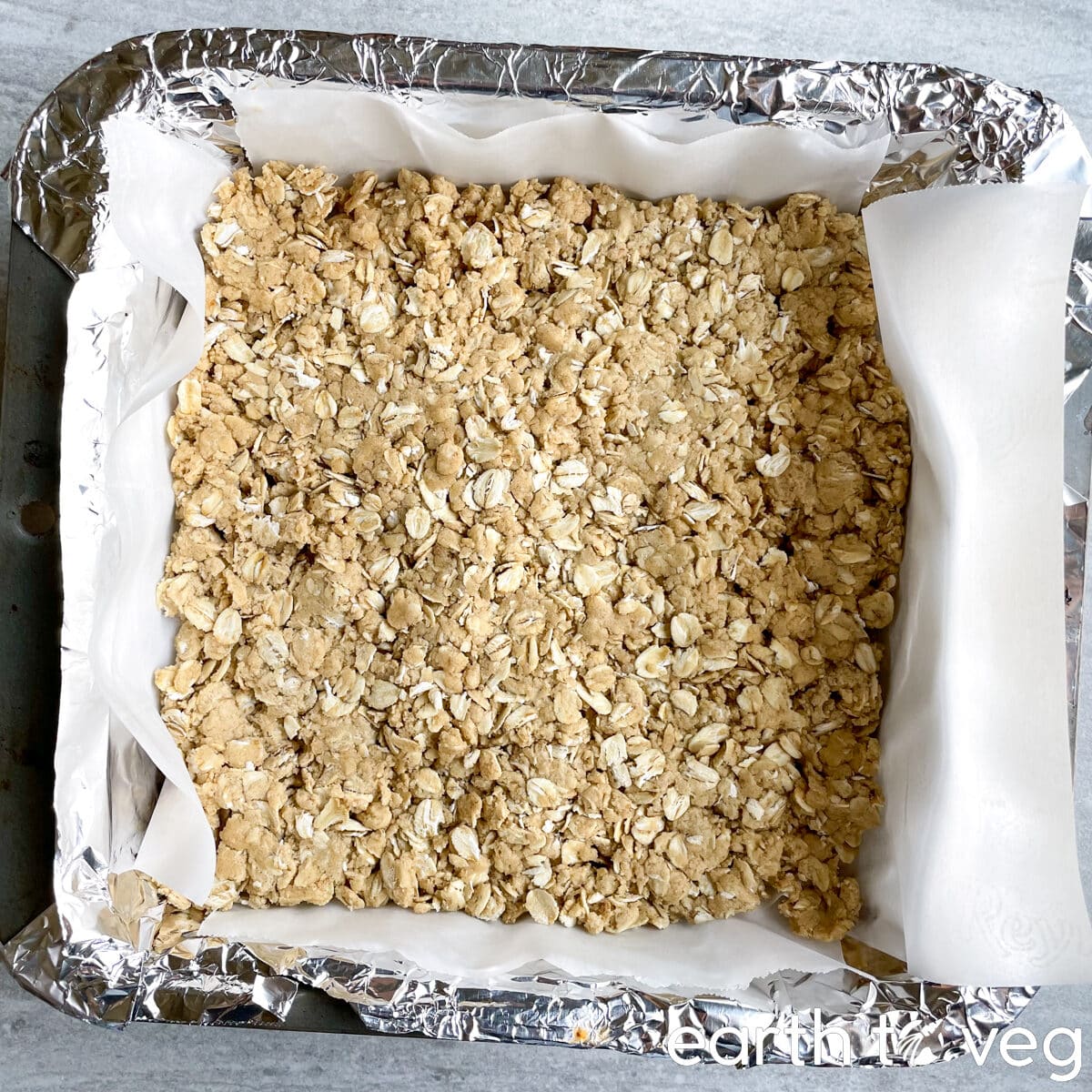 The first layer of oat-flour cake mixture is pressed into a square baking pan lined with foil and parchment paper.