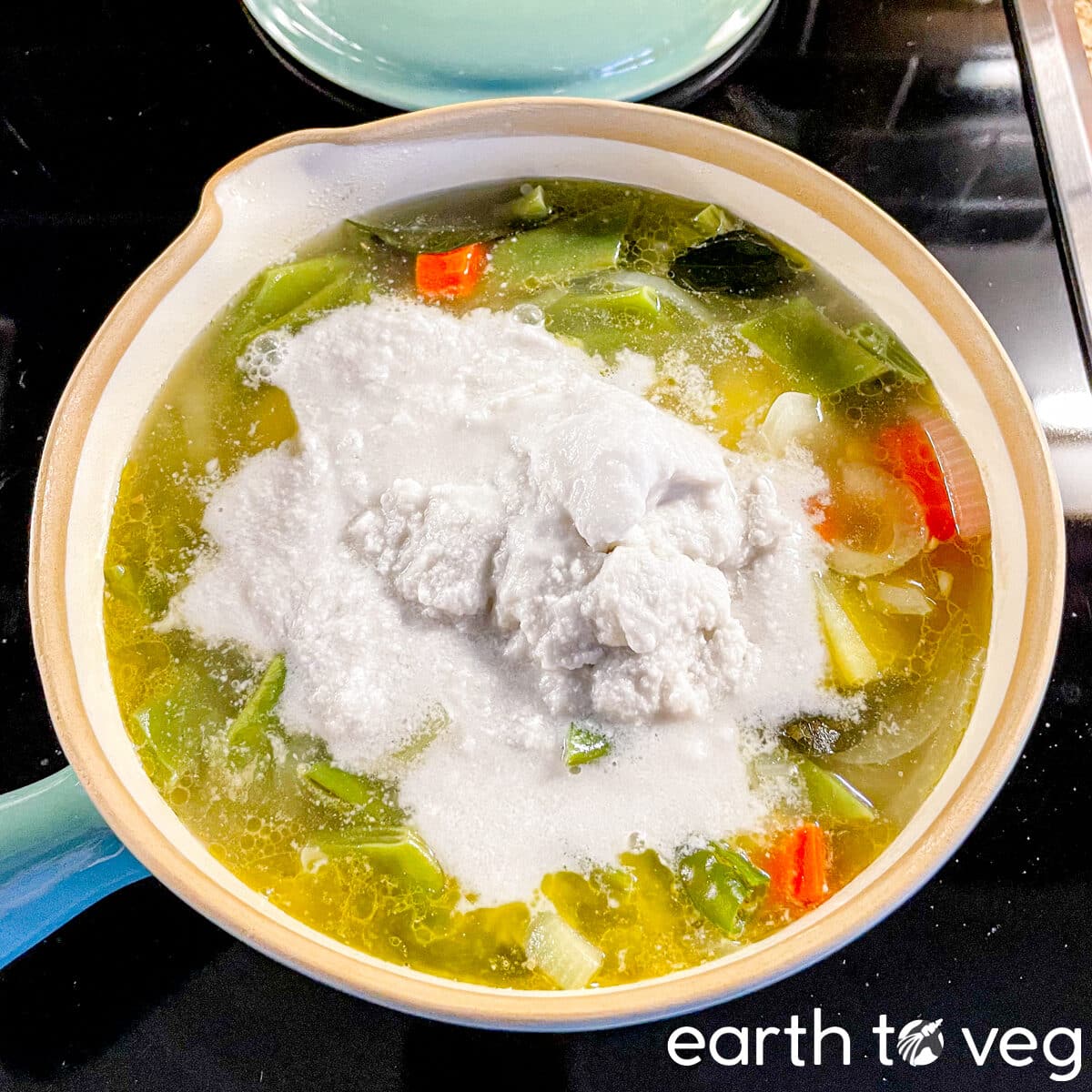 Coconut milk is poured onto a pot of cooked vegetable ishtew.