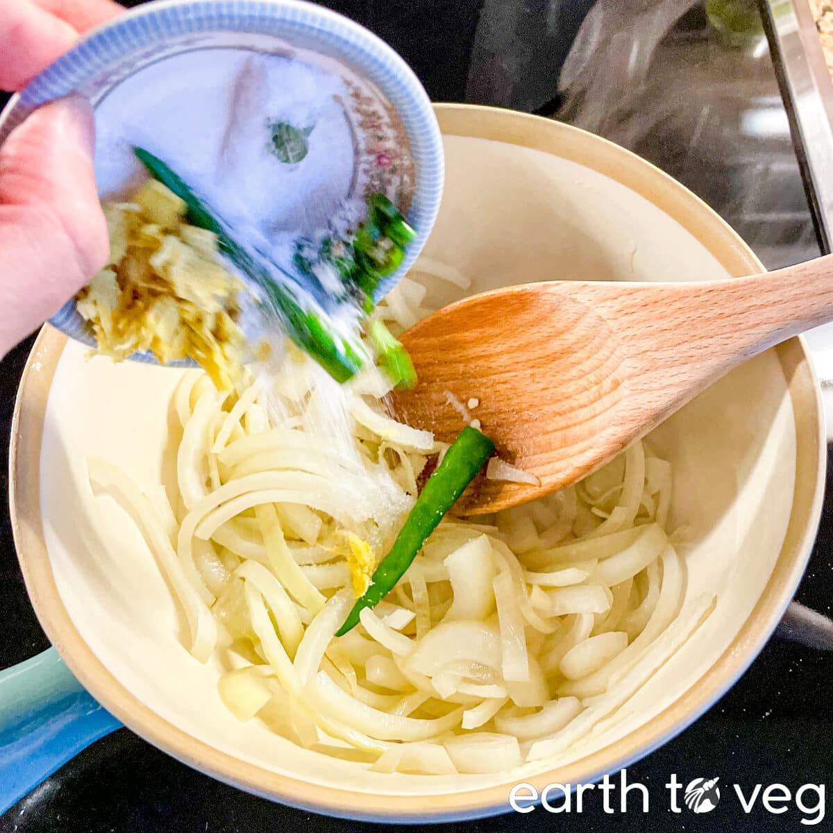 Chili pepper, ground ginger, and salt are added to cooking onions in a Dutch oven.