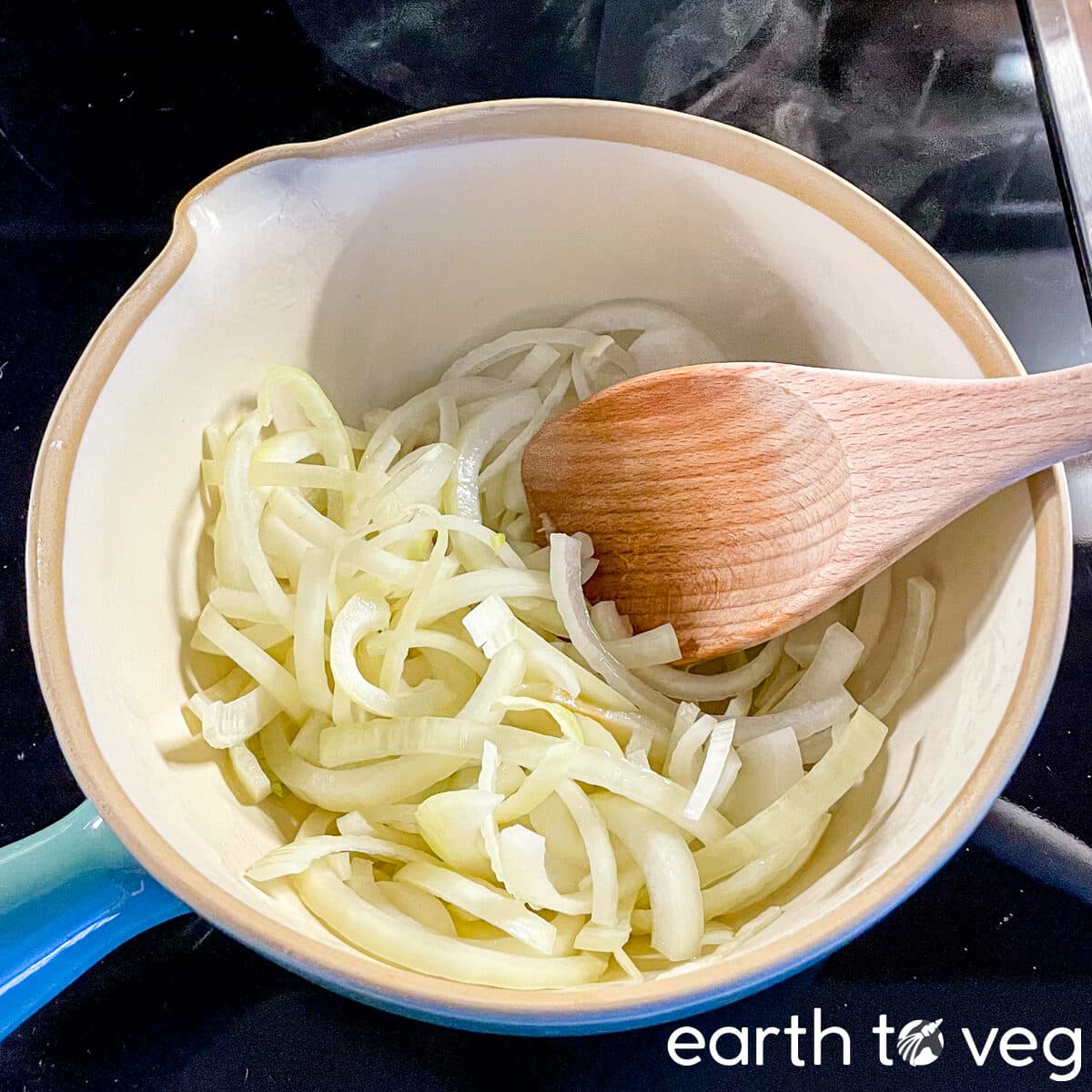 Yellow onions and wooden spatula in a teal-coloured Dutch oven.