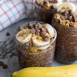 Chocolate banana chia pudding in a glass cup on a grey counter in front of a checkered white cloth.