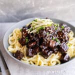 Vegan jajangmyeon in a bowl with chopsticks on the side, topped with julienned cucumber and sesame seeds.