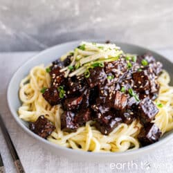 Vegan jajangmyeon in a bowl with chopsticks on the side, topped with julienned cucumber and sesame seeds.
