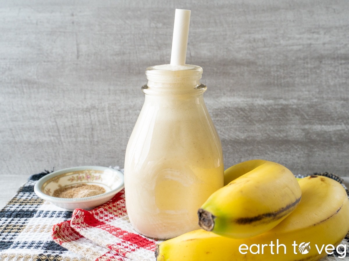 A small glass jar of banana licuado stands on a table covered with waffle dishcloths.