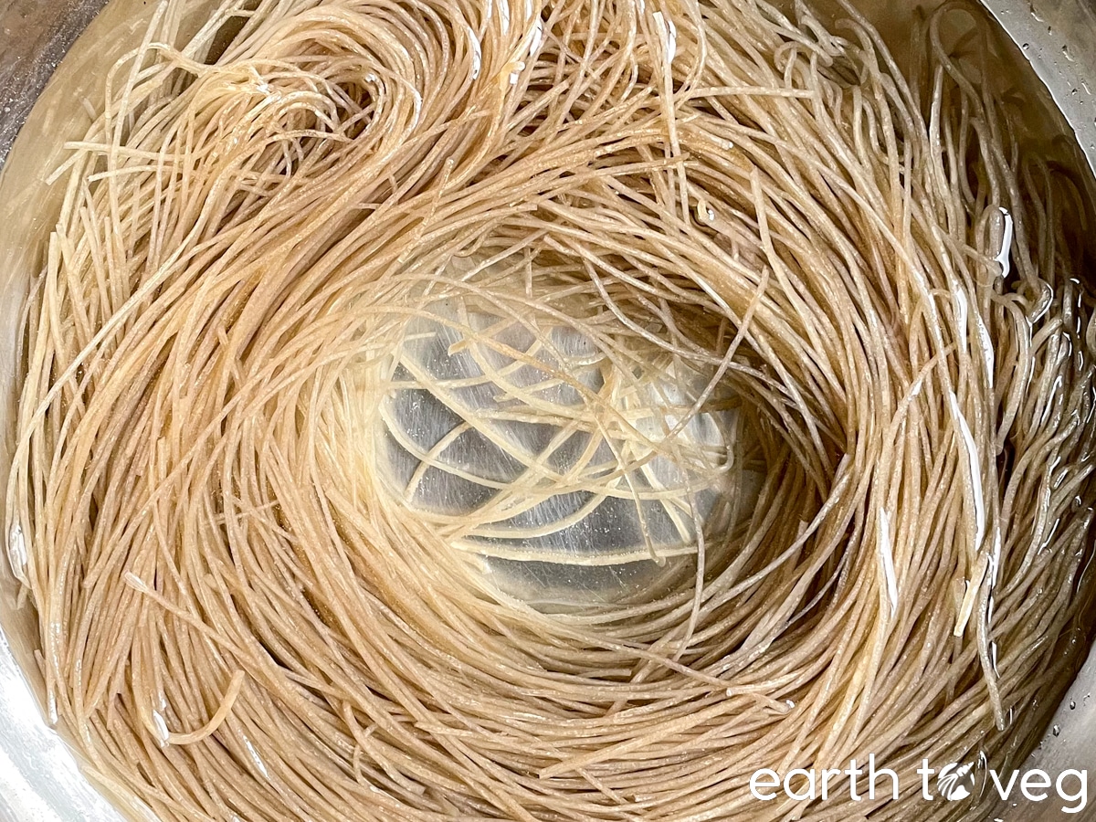 A large bundle of dangmyeon (sweet potato noodles) are soaked in a bowl of cold water.