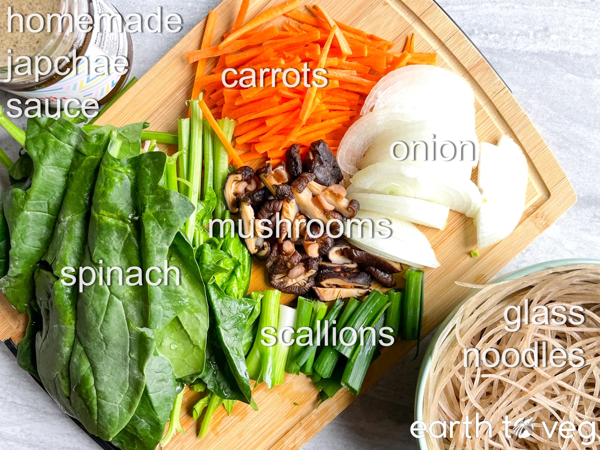 A top-down view of the japchae ingredients laid out on a wooden chopping board on grey counter.