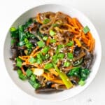 A bowl of japchae sits on a white table.
