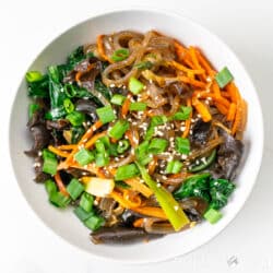 A bowl of japchae sits on a white table.