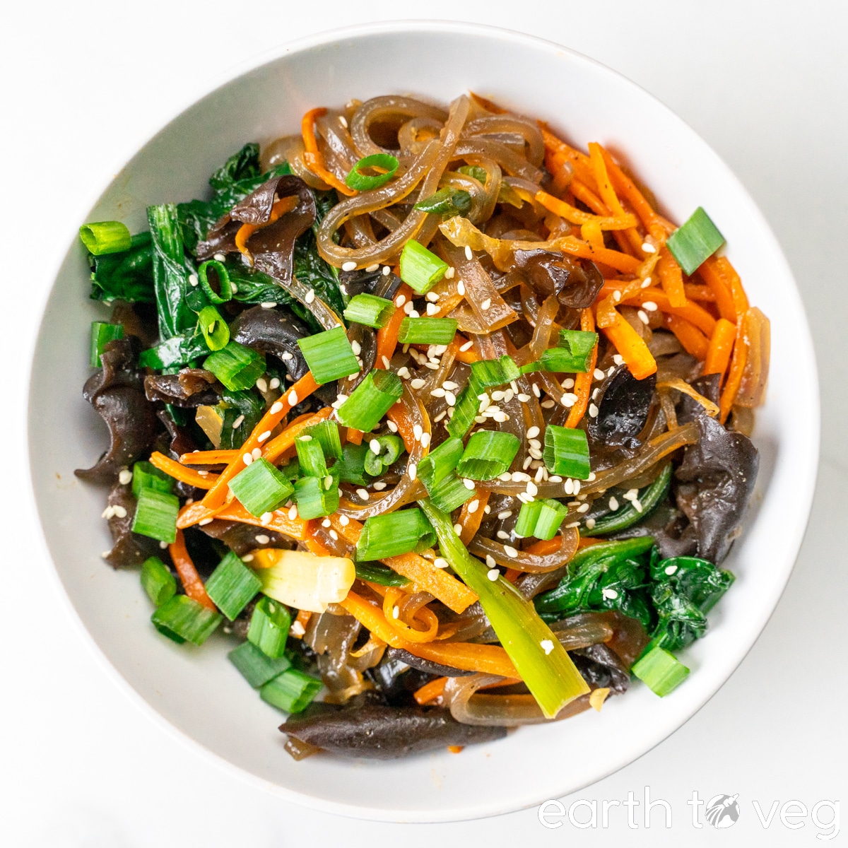 A bowl of japchae sits on a white table.