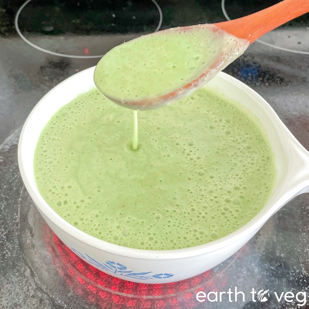 A wooden spatula stirs up a pot of pandan kaya mixture in a small saucepan.