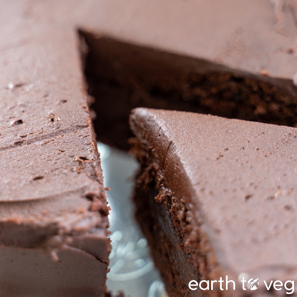 A closeup of a freshly iced and sliced chocolate cake on a glass cake stand.