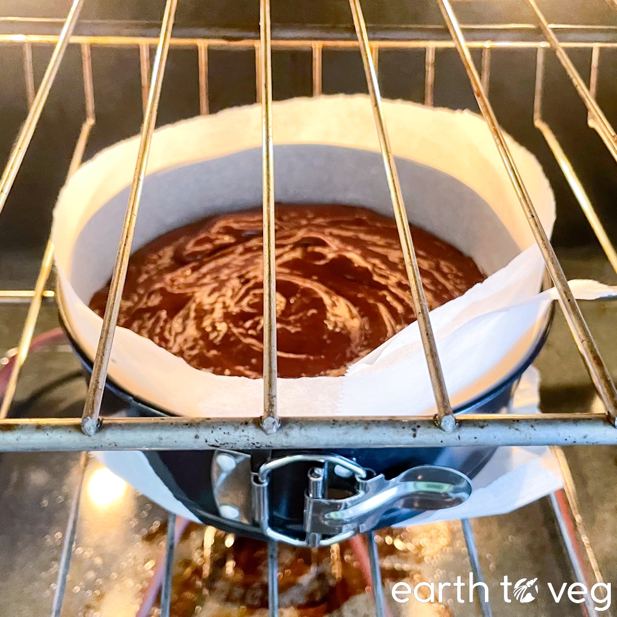 Chocolate batter in a round metal cake pan bakes inside of a conventional oven.