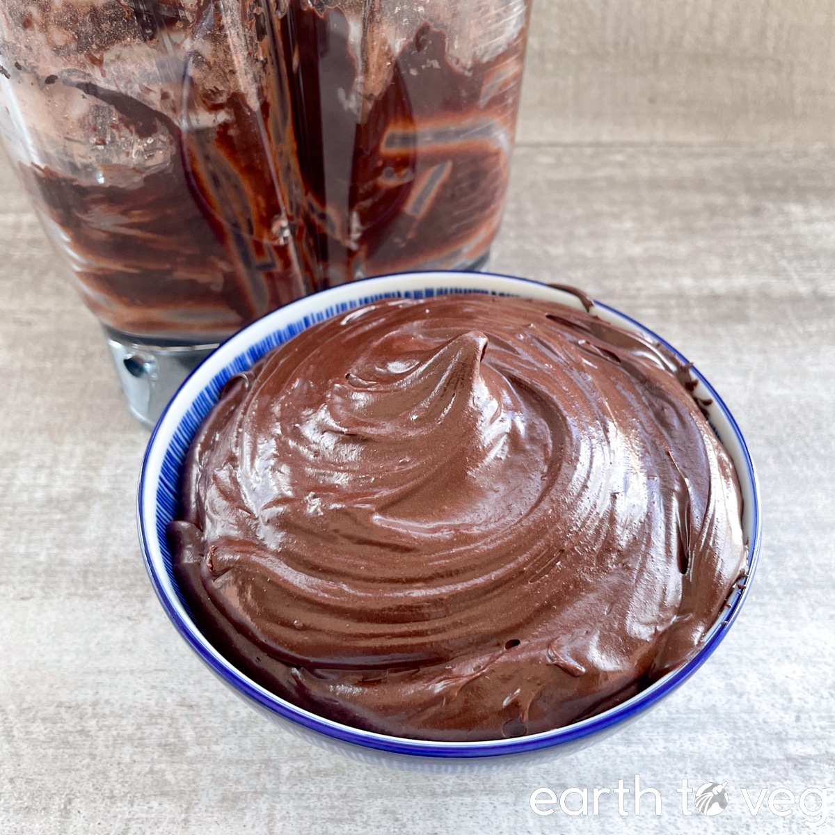 A glass measuring cup full of chocolate frosting on a granite counter, next to a blender jar that has been scraped empty.