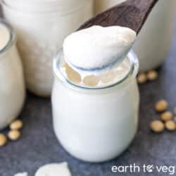 A wooden spoon lifts out a spoonful of creamy soy yogurt out of a small yogurt pot.
