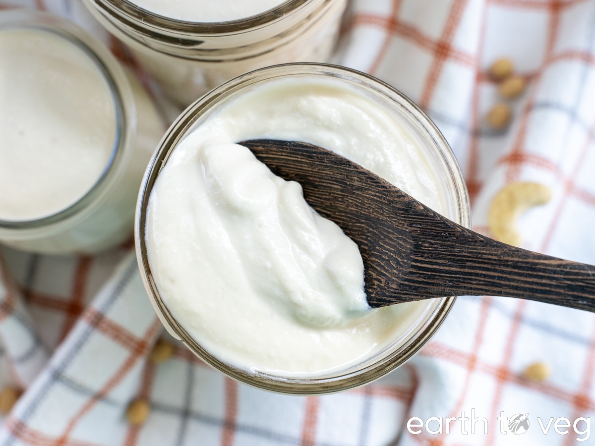 A wooden spoon scoops soy cashew yogurt from a glass mason jar.