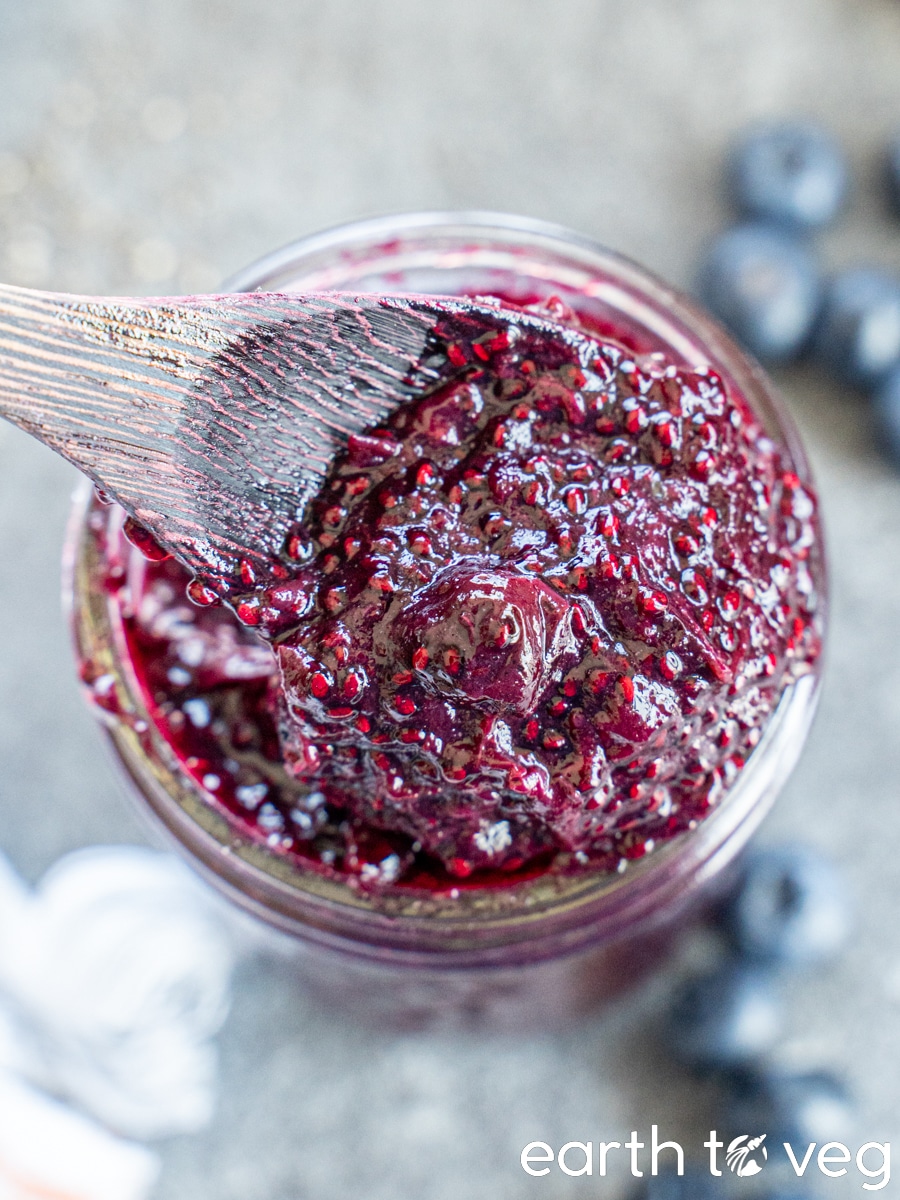 Blueberry chia seed jam is stirred around in a glass jar with a wooden spoon.