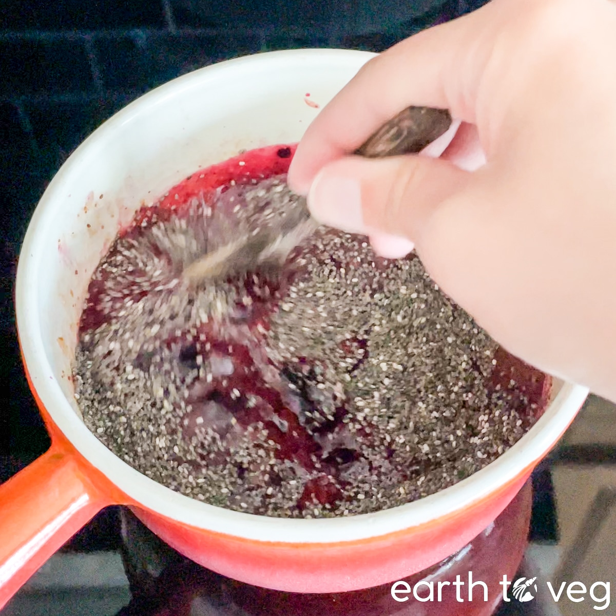 Chia seeds are stirred into cooked blueberries in a small saucepan.