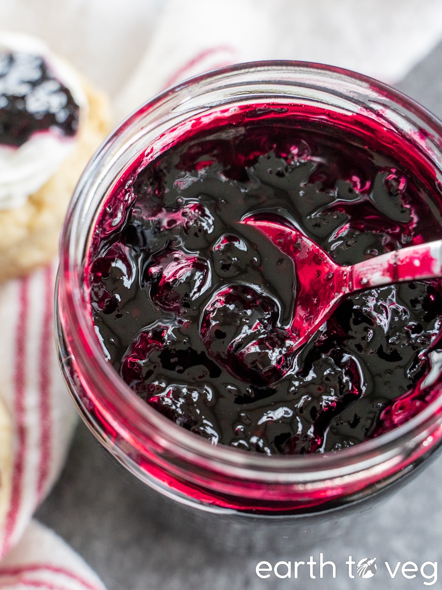 A metal spoon scoops from a glass jar of honeyberry jam.