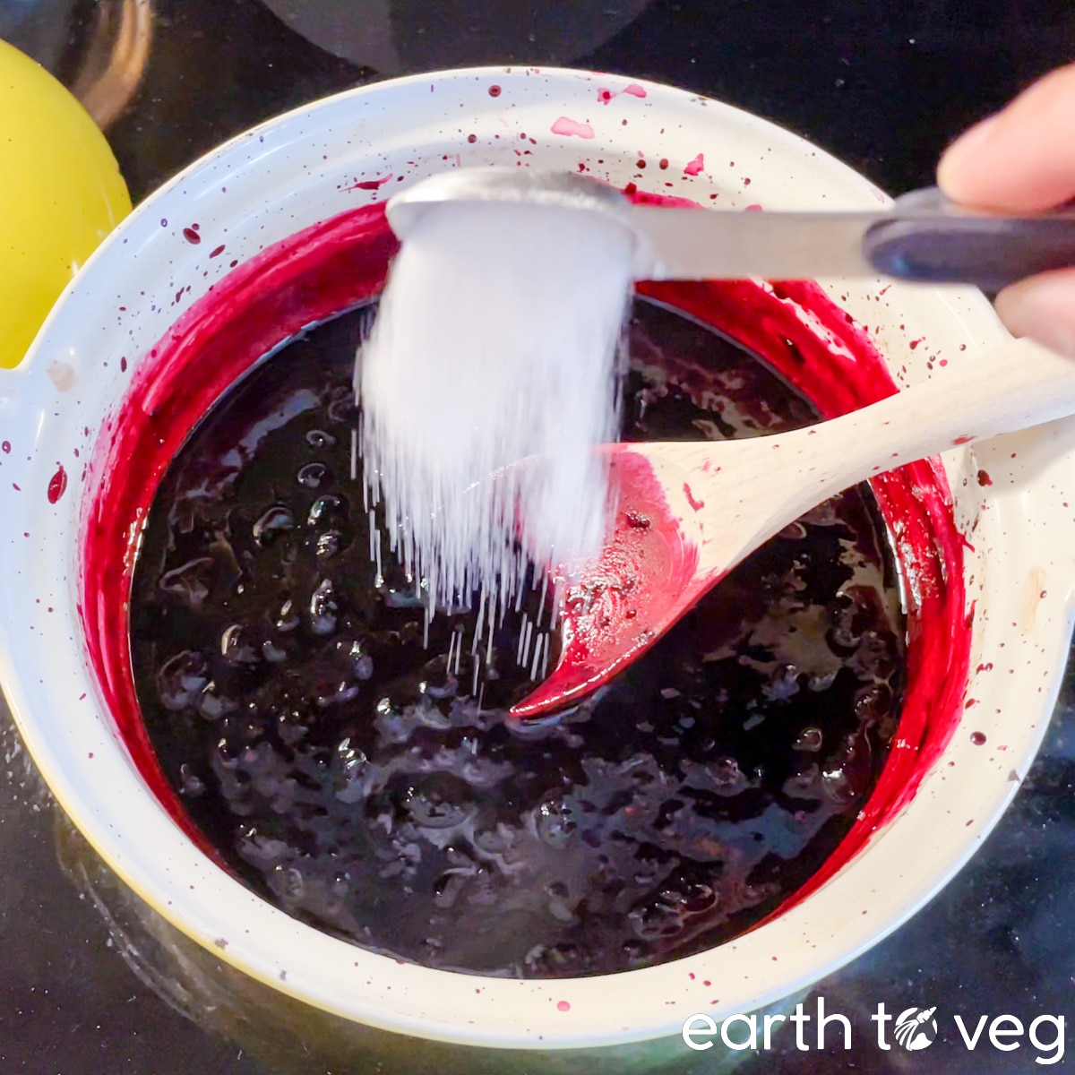 A 1/4 teaspoon of citric acid being poured into a pot of haskap jam.
