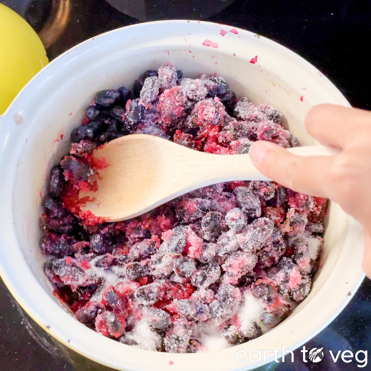 A wooden spatula is used to mash haskap berries and sugar together in a Dutch oven.