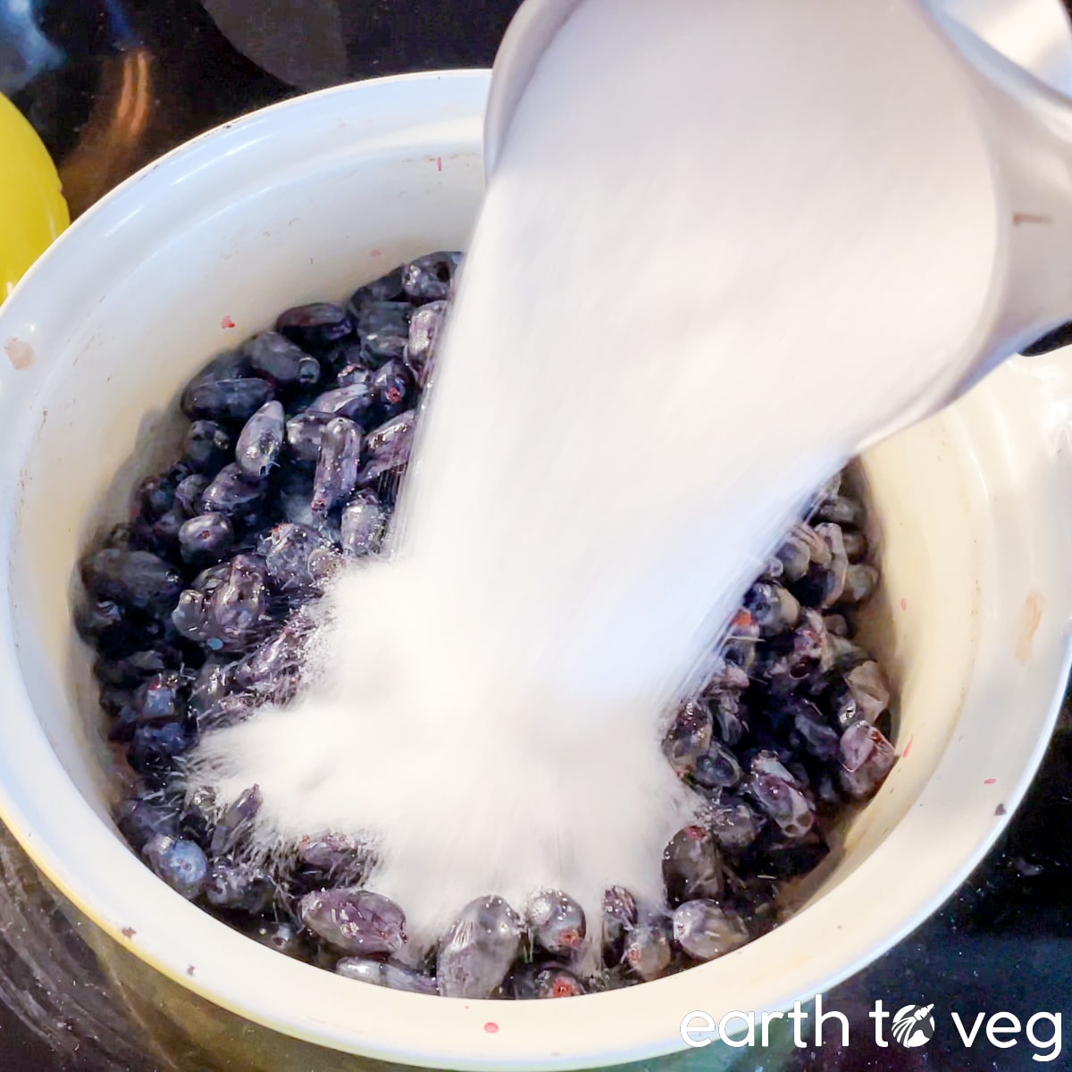 1 cup of white sugar is poured into a Dutch oven filled with fresh honeyberries.