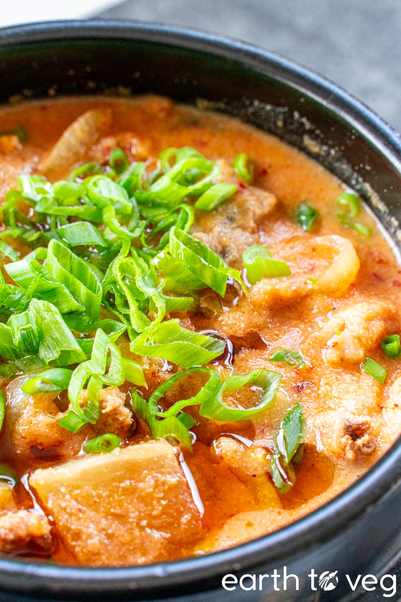 A bubbling pot of kongbiji jjigae topped with chopped scallions on a grey countertop.