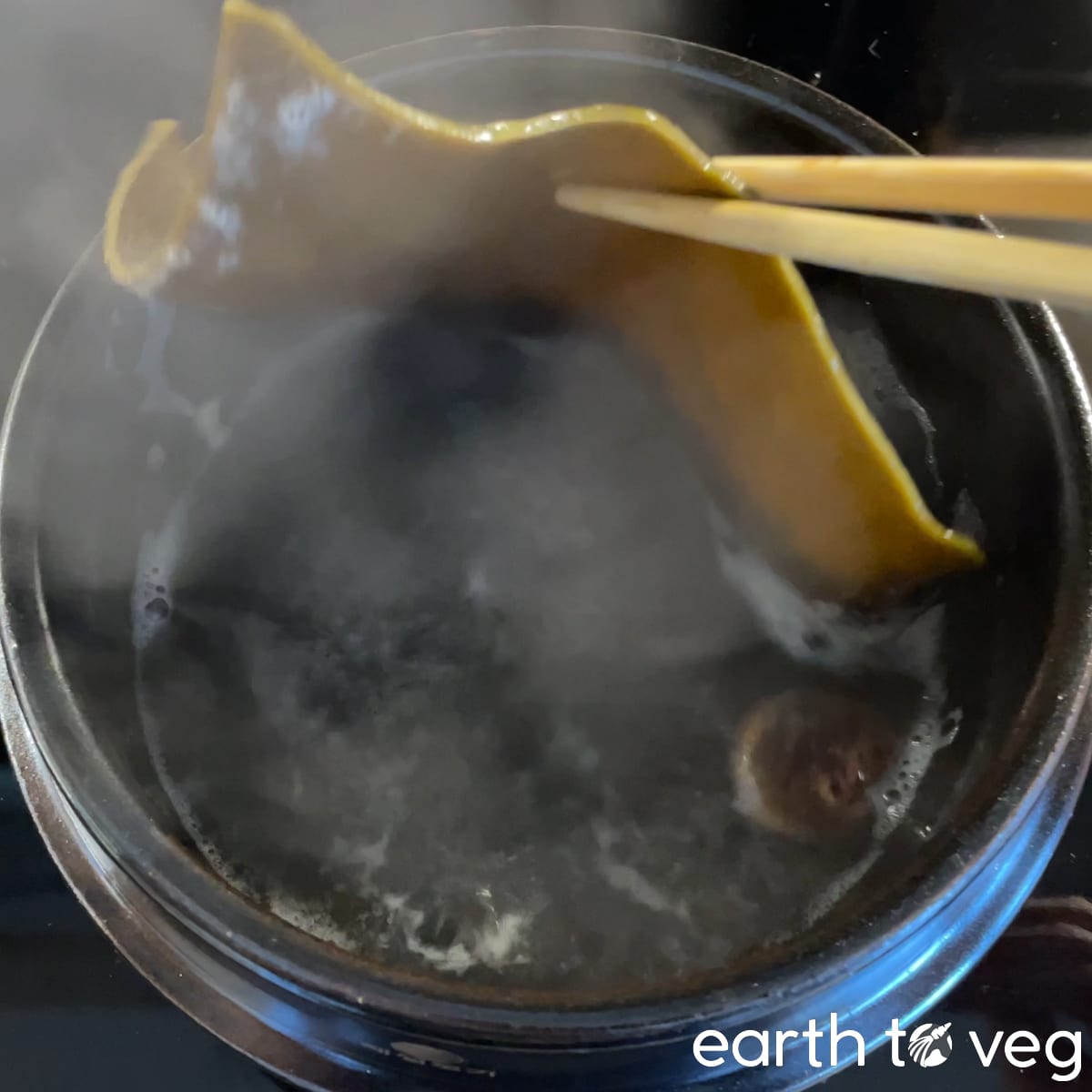 Boiled kombu is removed from a boiling pot of yuksu stock with chopsticks.