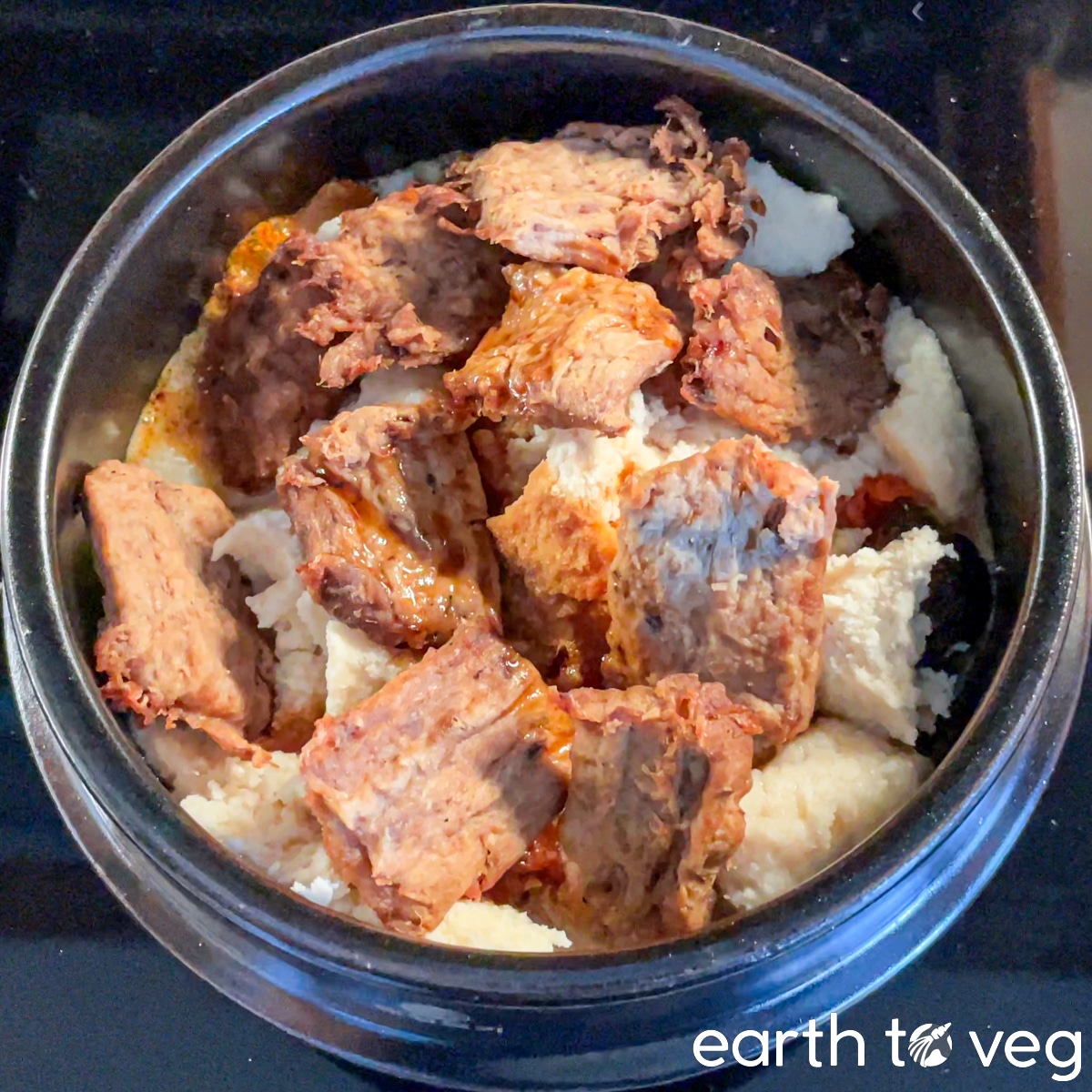 Okara and vegan beef layered over a bed of kimchi and yuksu stock in a small ttukbaegi.