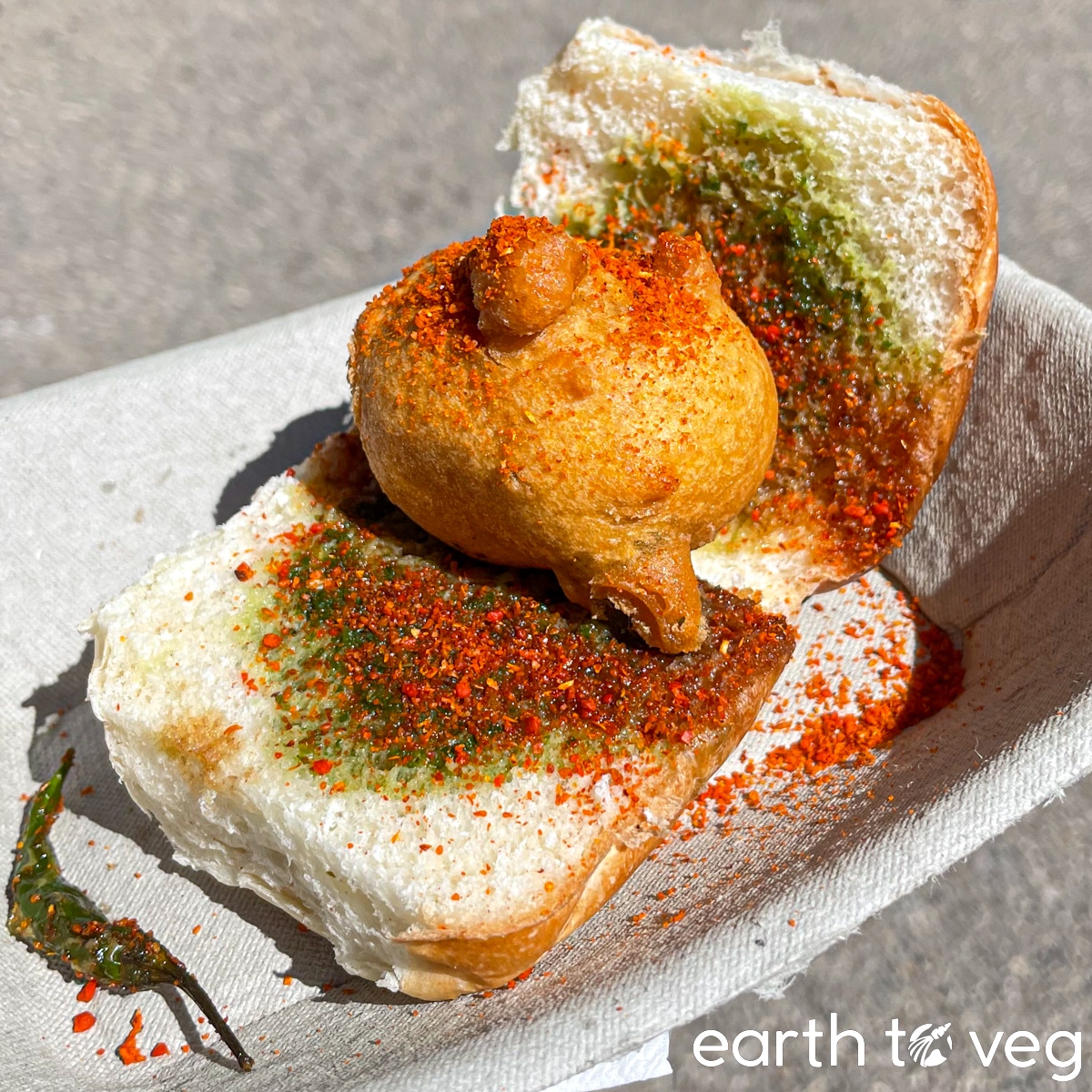 Small vada pav laying open-faced on a compostable cardboard plate.