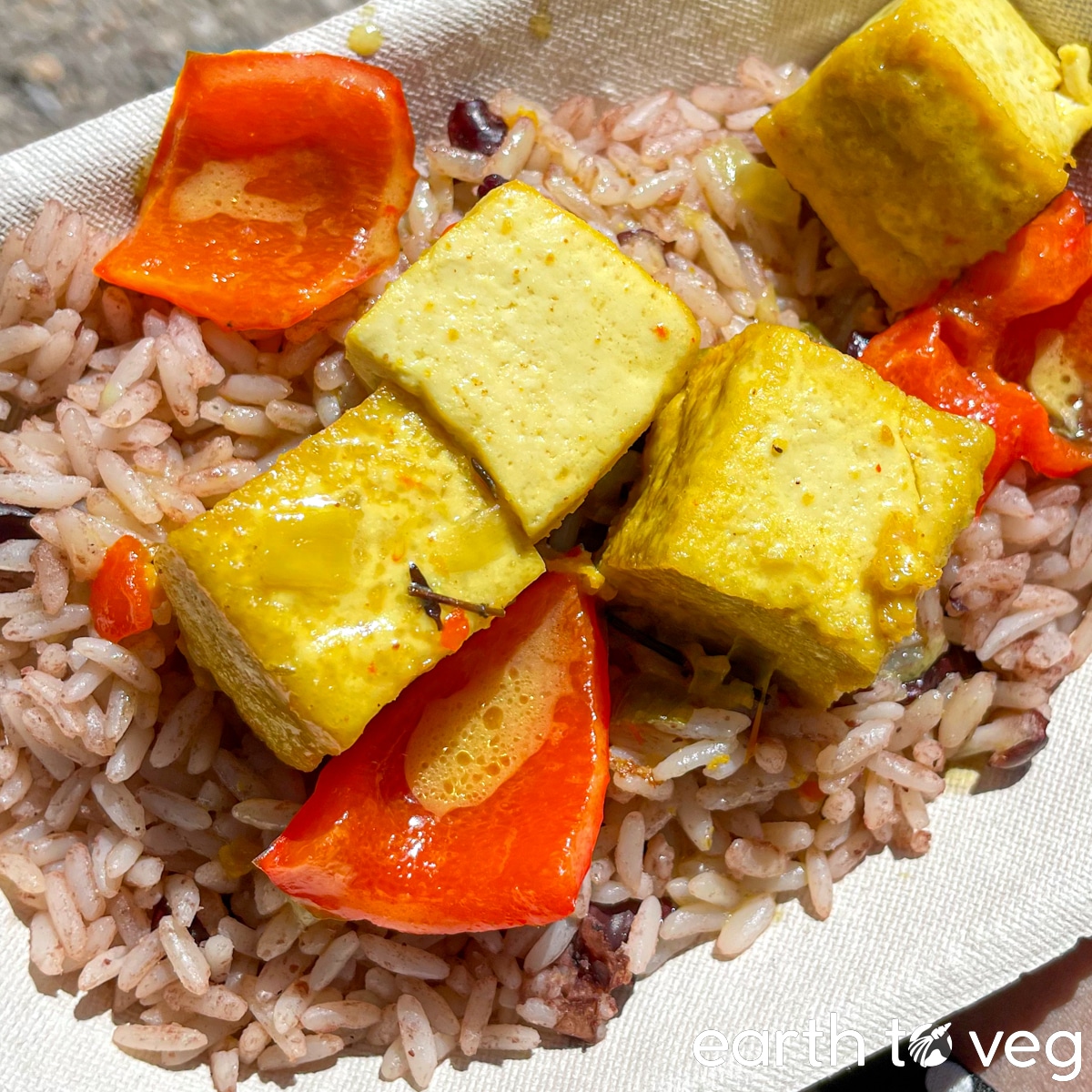 Four pieces of Jamaican curry tofu and sliced red bell peppers on a bed of coconut brown rice.