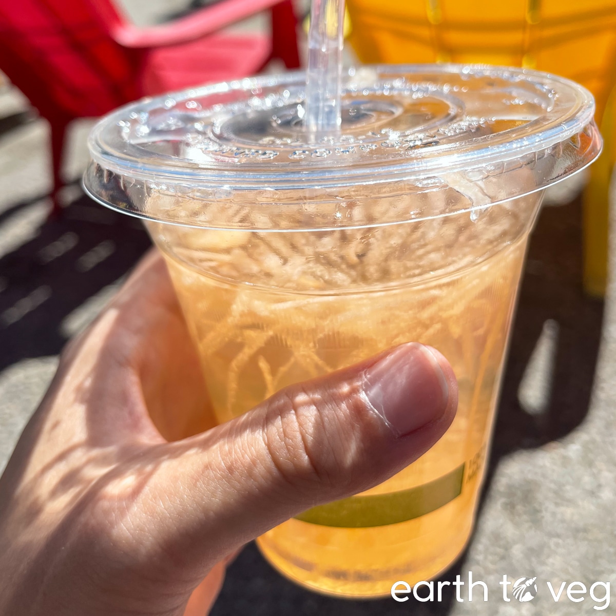 Hand holds up a plastic tumbler of cantaloupe juice.