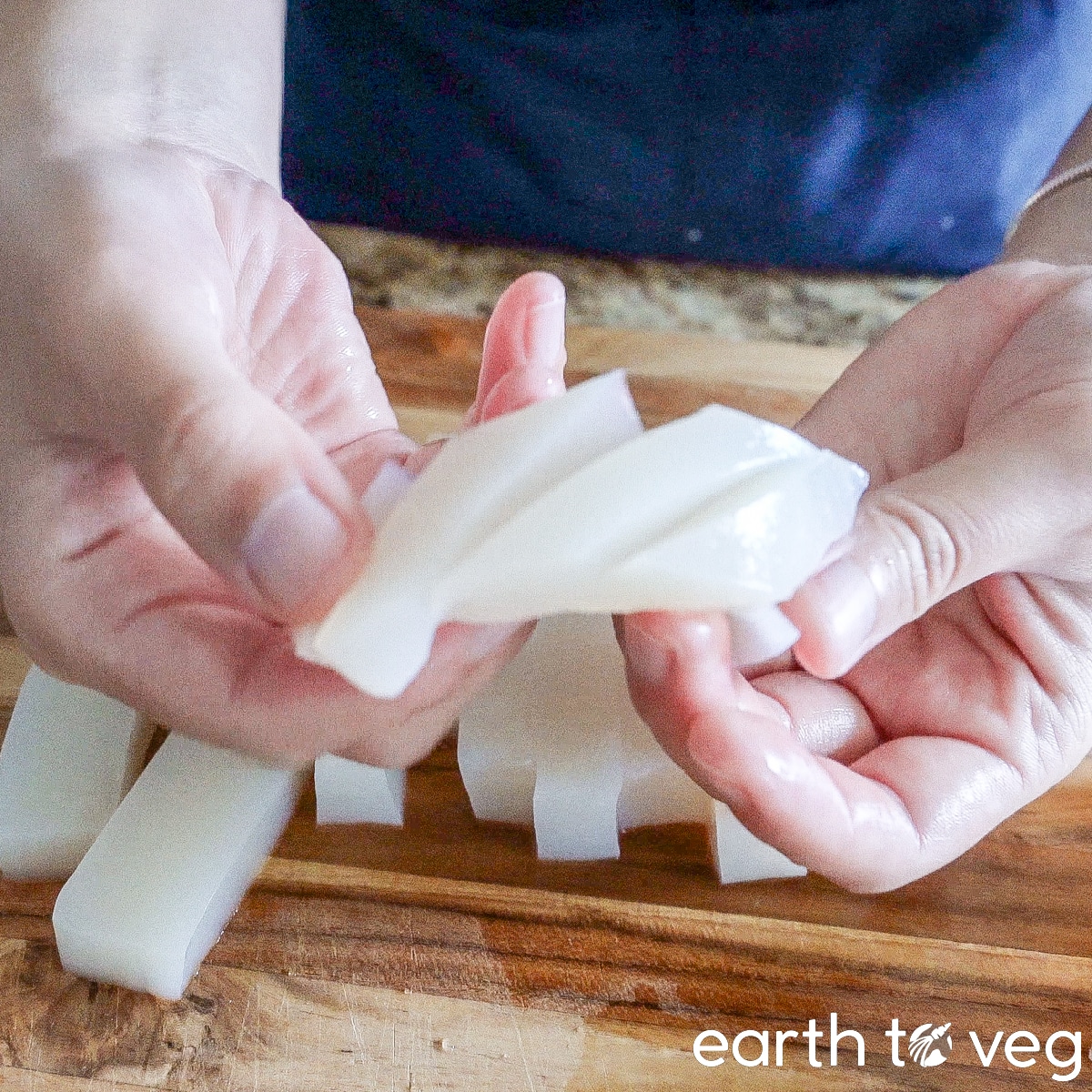 Hands hold up a piece of scored konnyaku.
