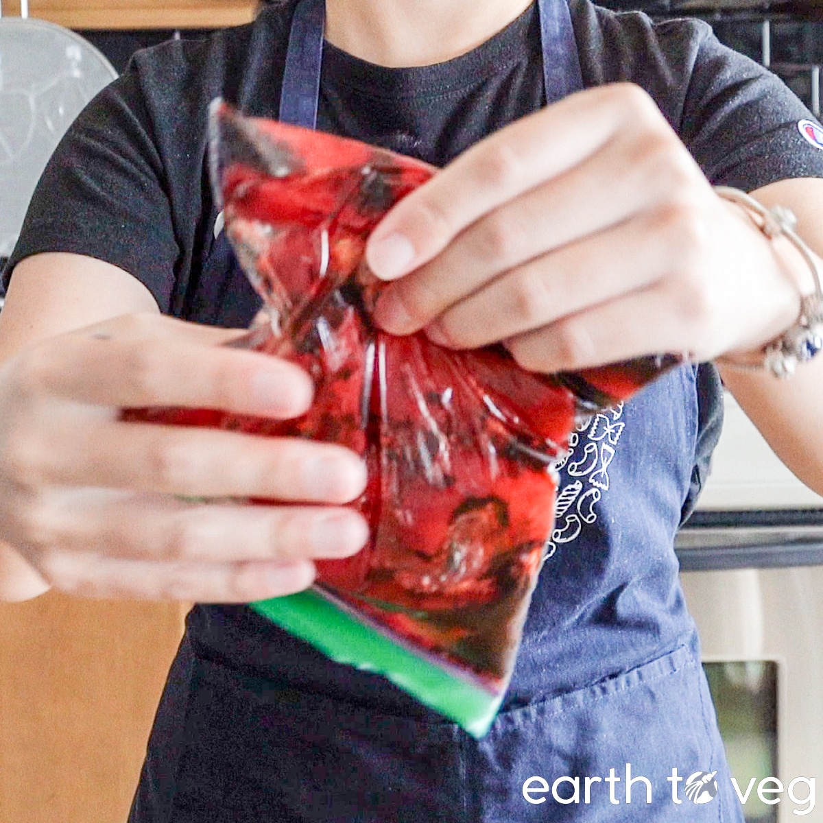 A small Ziploc bag filled with konnyaku pieces and marinade is massaged by a woman in a blue apron.