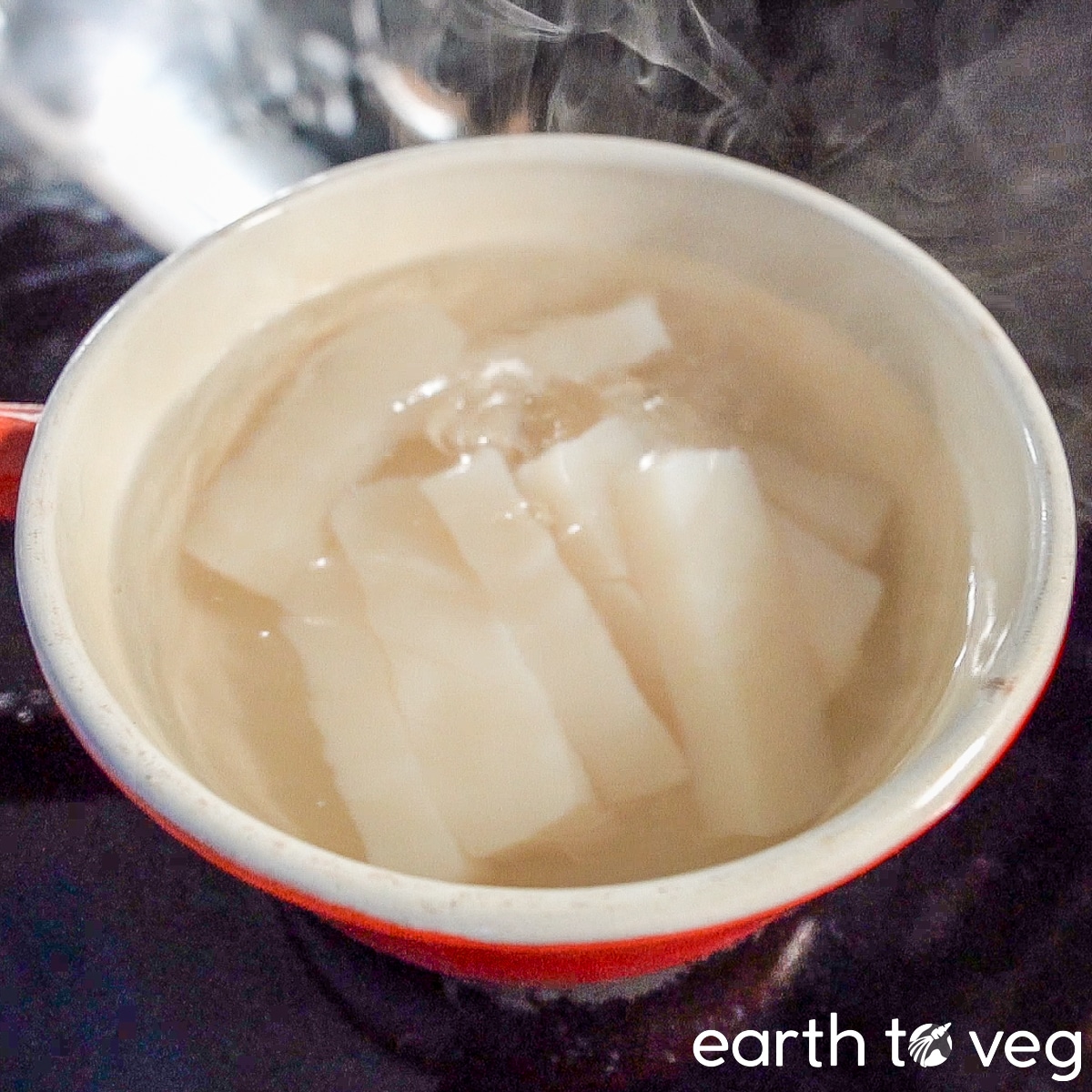 Slices of konjac yam cake are boiled in water in a small ceramic saucepan.