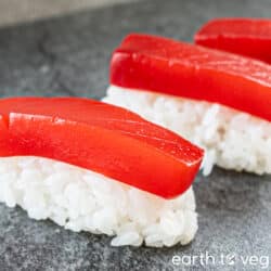 Three pieces of vegan salmon nigiri on a grey countertop.