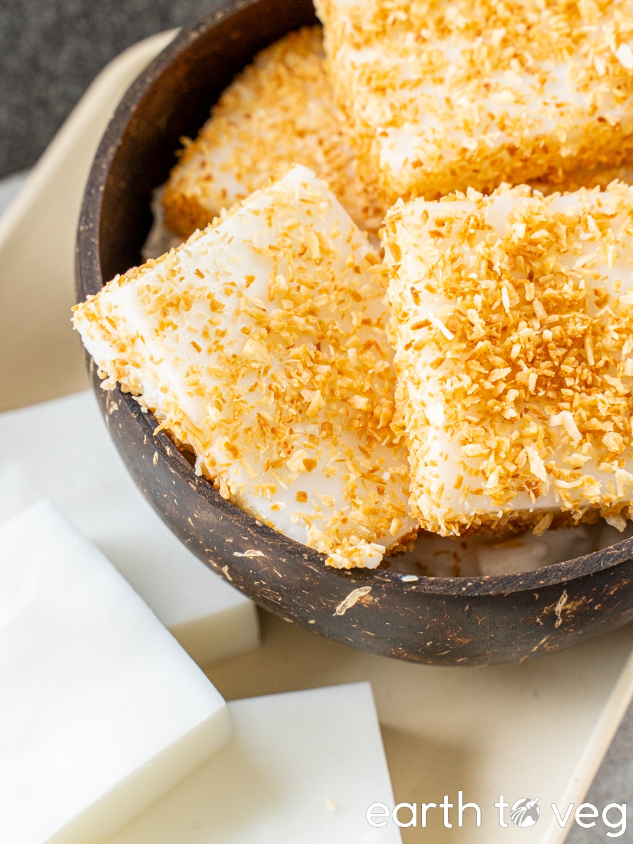 A coconut bowl full of haupia squares coated in toasted coconut flakes.