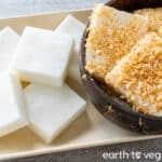 Plain haupia squares on a beige plate next to a coconut bowl full of toasted haupia.