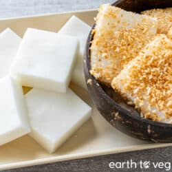Plain haupia squares on a beige plate next to a coconut bowl full of toasted haupia.