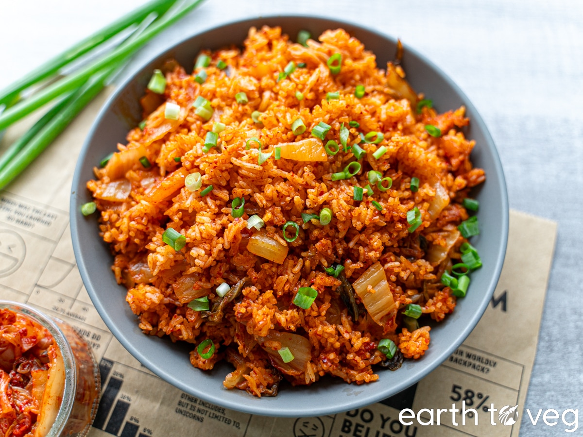 A large bowl of kimchi rice sprinkled with chopped green onion on a grey countertop.