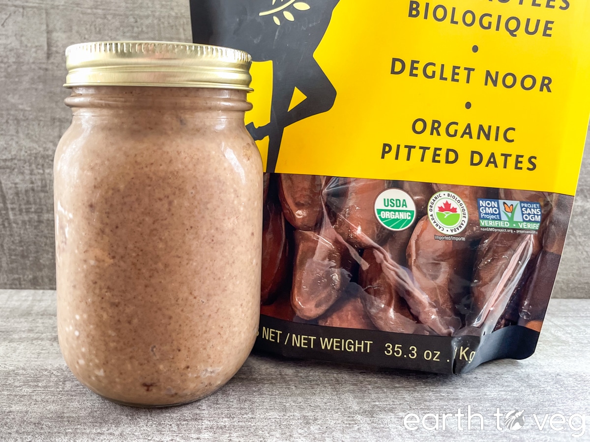 A mason jar full of homemade peanut butter on a grey countertop next to a bag of organic Deglet Noor dates.