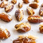 Peanut butter stuffed dates sprinkled with coconut and flaky sea salt on a sheet of wax paper.
