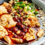 Spicy Sichuan doufunao (tofu pudding) submerged in a soy-chili based sauce, topped with green onions and peanuts.