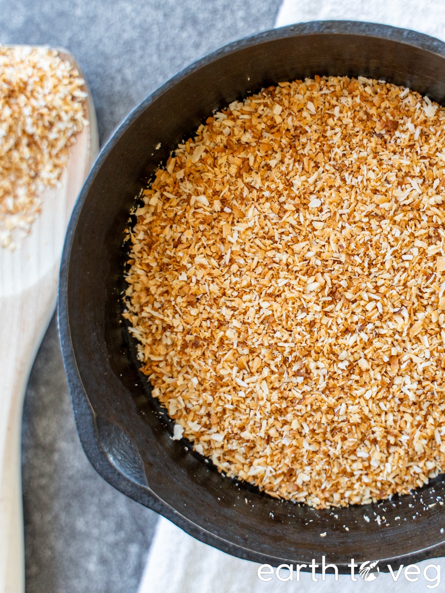 Golden-brown coconut shreds in a cast-iron skillet on a grey countertop.