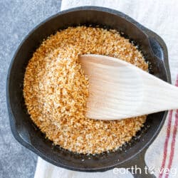 A wooden spatula stirs up a cast iron skillet full of shredded toasted coconut.