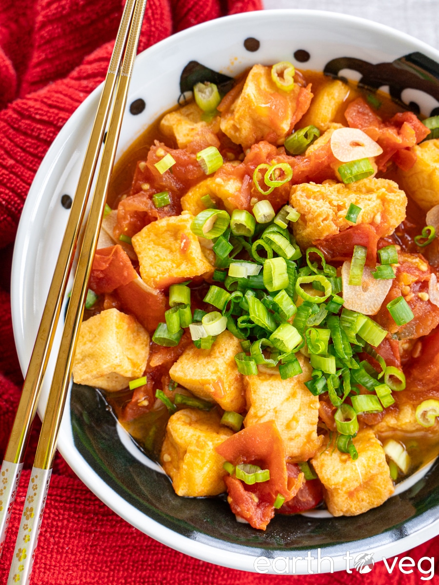 A bowl of Vietnamese tofu puffs in tomato sauce rests on top of a red cotton towel, accompanied by a pair of chopsticks.