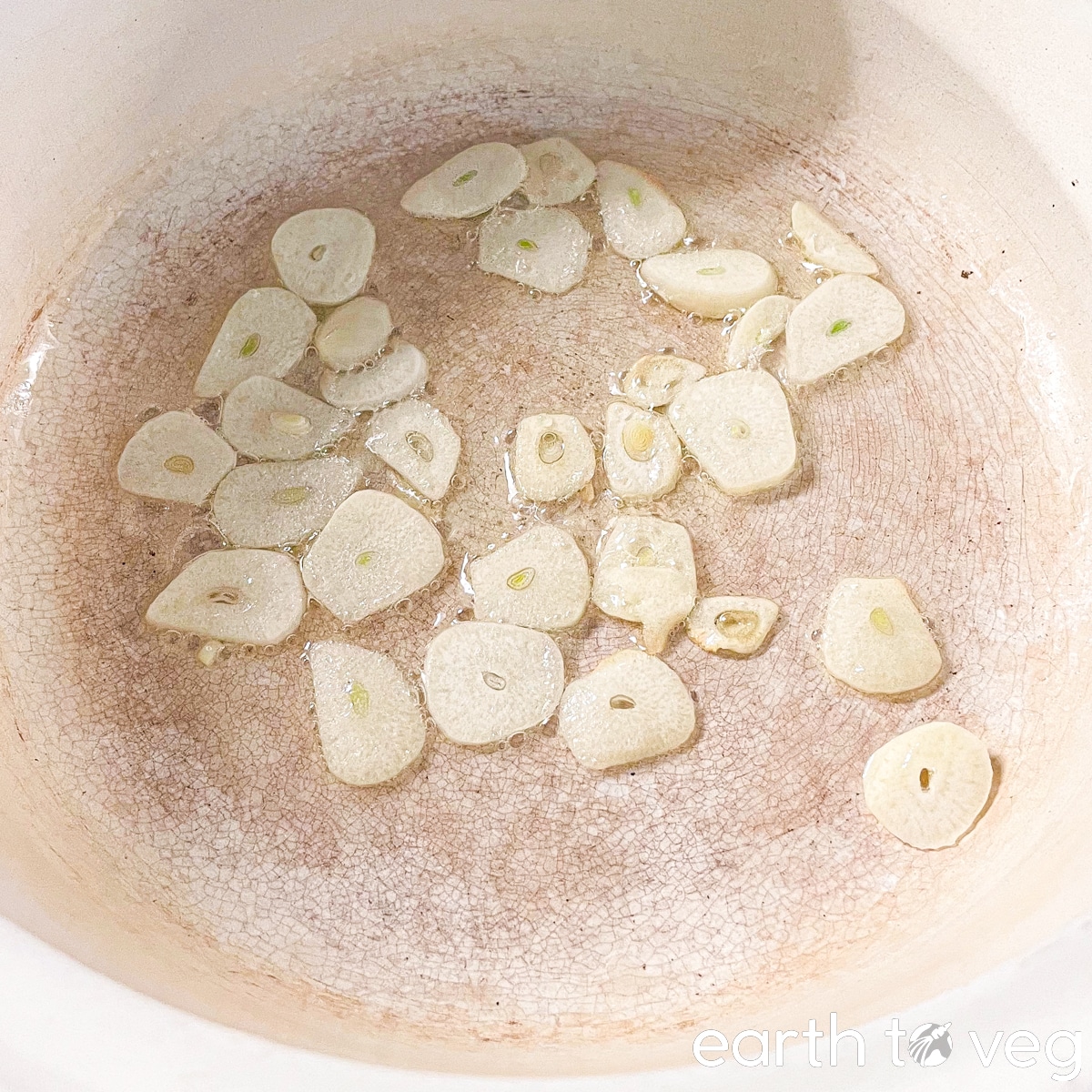Thin garlic slices are sizzling in a light layer of oil in an enameled Dutch oven.